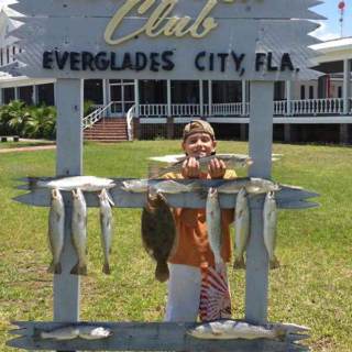 A kid holding up his fish in front of Rod & Gun Club