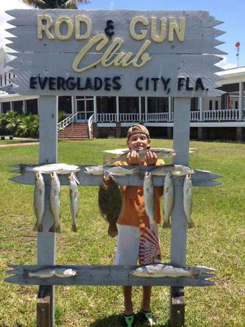 A kid holding up his fish in front of Rod & Gun Club